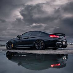 a black sports car parked on the side of a road with dark clouds in the background