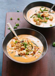 two bowls filled with soup and garnished with vegetables on a wooden table top