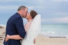 a bride and groom kissing on the beach