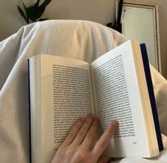 a person laying in bed reading a book with their hand on top of the book