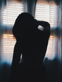 the silhouette of a woman standing in front of a window with sheer curtains on it