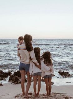 three girls are standing on the beach with their arms around each other as they look at the water