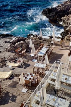 an outdoor dining area with tables and chairs near the water's edge, overlooking the ocean