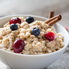 oatmeal with berries and cinnamon sticks in a white bowl on a table