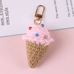 a crocheted ice cream cone keychain on a pink surface with a white piece of paper in the background