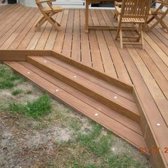 a wooden deck with steps leading up to a table and chairs on the grass next to it