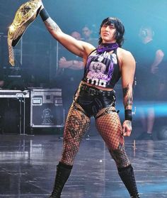 a woman in fishnet tights holds up a snake on stage with other people behind her