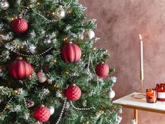 a christmas tree decorated with red and silver baubles next to a lit candle