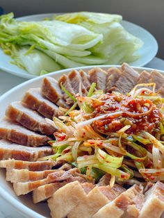 a white plate topped with meat and veggies next to another plate filled with lettuce