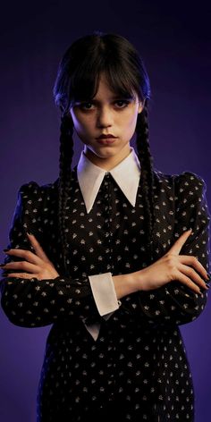 a woman with her arms crossed wearing a black and white polka dot dress, standing in front of a purple background