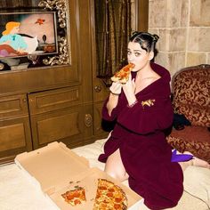 a woman in a bathrobe eating pizza on the floor next to a couch