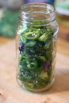 a glass jar filled with green peppers on top of a wooden table