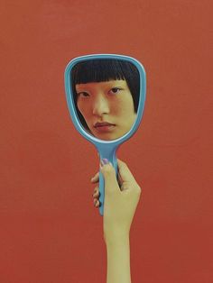 a woman's hand holding a blue mirror with her face in it, against a red background