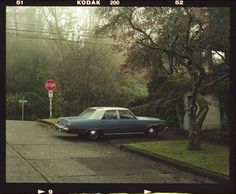 an old car is parked in front of a stop sign on the side of the road