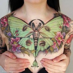 a woman with tattoos on her chest holding a butterfly in front of her stomach and breast