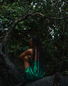 a woman sitting on top of a tree branch in the forest wearing a green dress