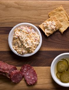 several different types of food in bowls on a wooden table with crackers and olives