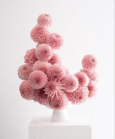 a white vase filled with pink flowers sitting on top of a white table next to a wall