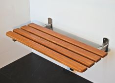 a wooden bench mounted to the side of a white tiled wall next to a black tile floor