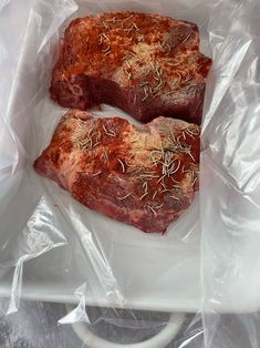 two pieces of steak sitting on top of plastic wrapped in cellophane and sprinkled with seasoning