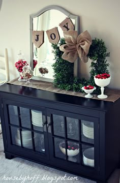 a black china cabinet with christmas decorations on top and a mirror above it that says joy