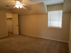 an empty room with a ceiling fan and carpeted flooring in front of the window