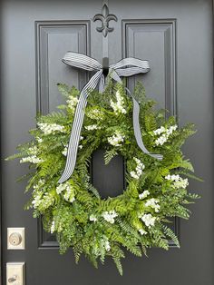 a green wreath with white flowers and a bow hanging on a gray front door,