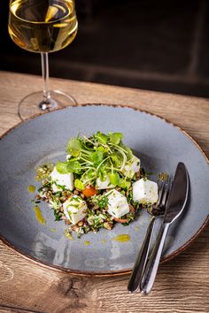 a blue plate topped with salad next to a glass of wine on top of a wooden table