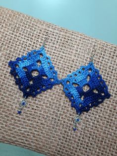 two blue crocheted square shaped earrings on a piece of fabric