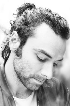 a man with curly hair and piercings looks down at his cell phone while wearing a leather jacket