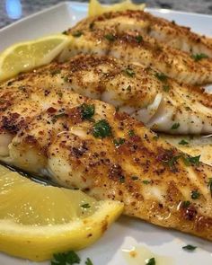 two fish fillets on a white plate with lemon wedges