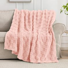 a couch with a pink blanket on top of it next to a potted plant