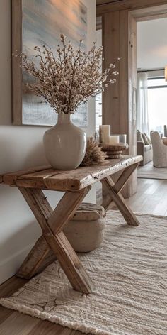 a wooden table topped with a white vase filled with flowers next to a painting on the wall