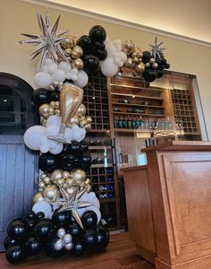 a large balloon arch is decorated with black, white and gold balloons