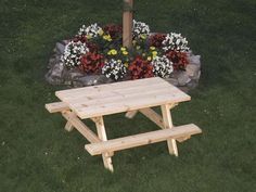 a wooden picnic table sitting in the middle of a grass covered field next to flowers