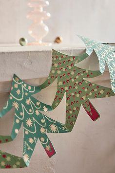 three paper christmas trees hanging from a window sill in front of a white wall