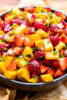 a fruit salad with strawberries and mangoes in a bowl next to tortilla chips