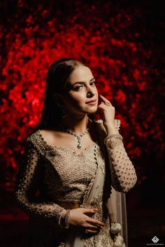 a woman in a white and gold lehenga standing against a red background with her hands on her face