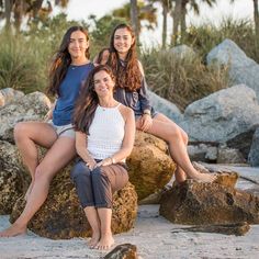 three women sitting on rocks in front of palm trees