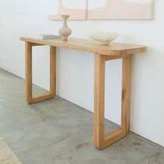 a wooden table with a vase on it next to a white wall and paintings behind it