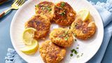 a white plate topped with crab cakes next to lemon wedges and a fork on a blue table cloth