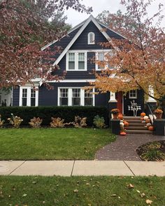 a black house with white trim and pumpkins on the front porch, in autumn