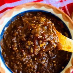 a wooden spoon full of chili sauce in a blue bowl on a red and white tablecloth