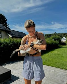 a woman holding two cats in her hands while standing on a wooden deck next to a house