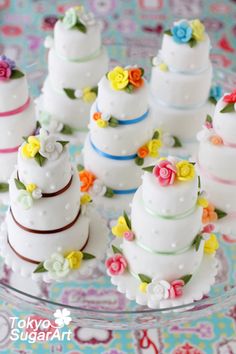 small wedding cakes are arranged on a glass platter with colorful flowers and ribbons around them