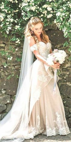 a beautiful woman in a wedding dress standing next to a stone wall with white flowers