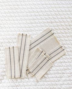 three pieces of cloth sitting on top of a white bed sheet with black and gray stripes