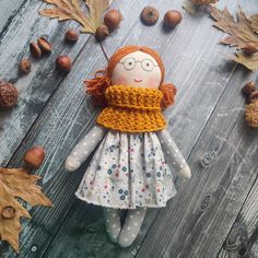 a doll with red hair and glasses is sitting on a wooden surface surrounded by autumn leaves