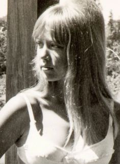 black and white photograph of a woman with long hair wearing a tank top, standing in front of a wooden fence