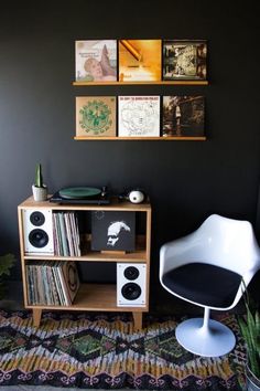 a white chair sitting next to a wooden table with records on top of it in front of a black wall